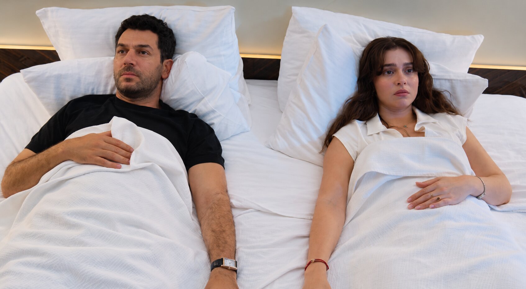 Murat Yıldırım as Serhat Tecer and Cemre Baysel as Zeynep Candan lying stiff in bed looking anxious toward the ceiling in Sins and Roses Season 2 (Güller ve Günahlar / Woroud Wa Thonoub).
